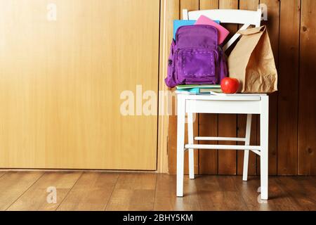 Backpack with school supplies on chair on wooden background Stock Photo