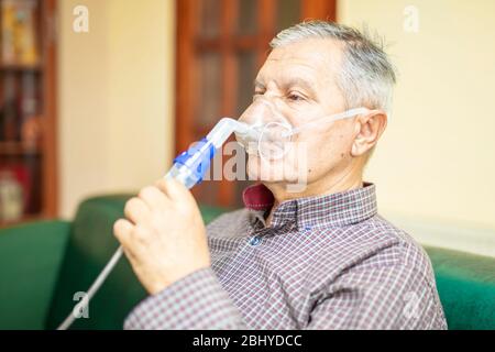 Senior man using medical equipment for inhalation with respiratory mask, nebulizer in the room Stock Photo