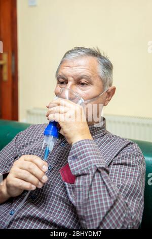Senior man using medical equipment for inhalation with respiratory mask, nebulizer in the room Stock Photo