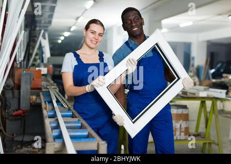 Portrait of man and woman worker who are standing with window frames in the pvc workshop. Stock Photo