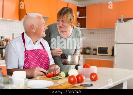 Cheerful senior couple enjoying time together at home, cooking vegetarian lunch in comfy kitchen Stock Photo