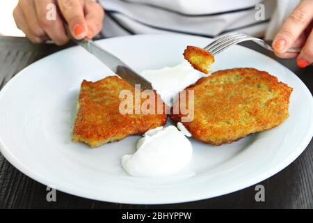 Female hands cutting potato pancakes with cream in plate on wooden table, closeup Stock Photo
