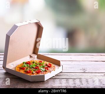 Pizza in box on wooden table on bright background Stock Photo