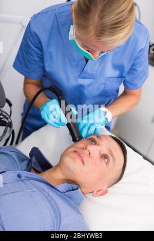 Woman doctor is doing vacuum massage procedure on face of adult client in clinic. Stock Photo