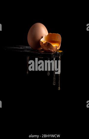 Concept image of a broken brown egg shell with dripping egg white on black background Stock Photo
