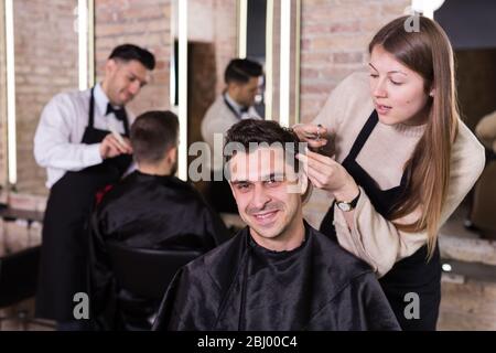 Handsome male client getting haircut by professional hairdresser in salon Stock Photo