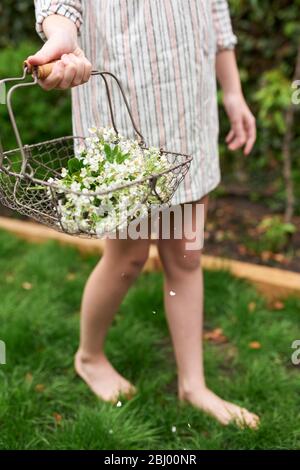 Young girl holding basket of flowers walking in garden.