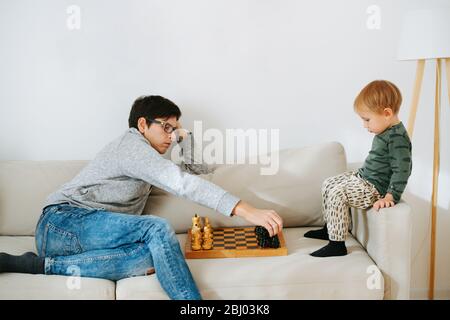 Father teaching his toddler son how to play chess on a sofa at home Stock Photo
