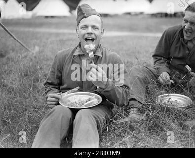 One of the civilian guests enjoying a meal. 15 young men from south London are spending a fortnight free holiday as guests of the 23rd London Regiment (the East Surrey) in annual camp at Arundel Park, Sussex. - 26 July 1937. - Stock Photo