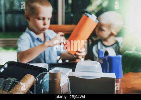 Different recycled materials on desk and blurred kids making crafts from it on the background. Zero waste and home scholling concept. Stock Photo