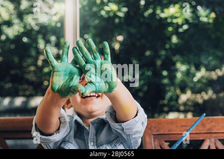 Boy with hands painted in green paints ready to make hand prints. Stock Photo