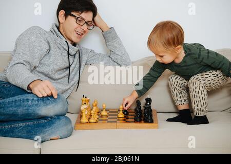 Father and his toddler son playing chess on a sofa at home Stock Photo
