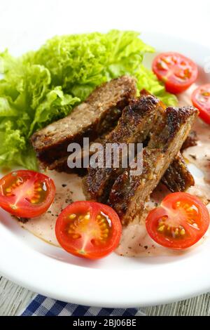 Tasty slices of meat with sauce and cherry tomato on plate close up Stock Photo