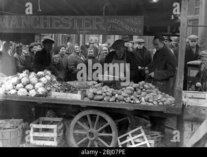 The weather brings a shortage of potatoes . The supplies of potatotes have been seriously menaced by the weather, owing to farmers being unable to open up clamps . A queue for potatoes at popular Sam Manchester 's stall seen at Beresford Square , Woolwich - 8 March 1947 Stock Photo