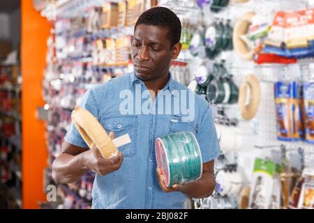 Portrait of concentrated adult seller of household goods shop organizing assortment of items on shelves and racks Stock Photo