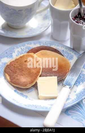 Home made Scotch pancakes (drop scones) at teatime with butter and raspberry jam and tea. Stock Photo