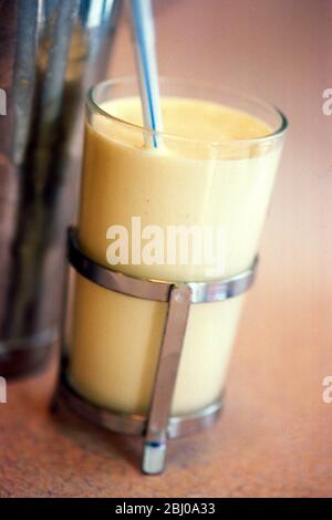 Banana milk shake in caged glass with striped straw on diner counter - Stock Photo