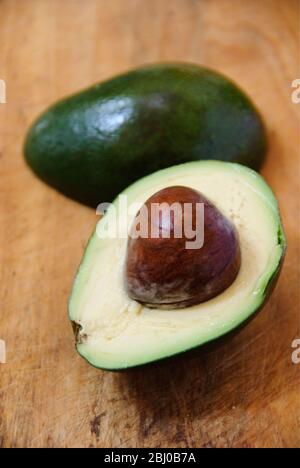 Whole and cut fresh avocado pear on wooden background - Stock Photo