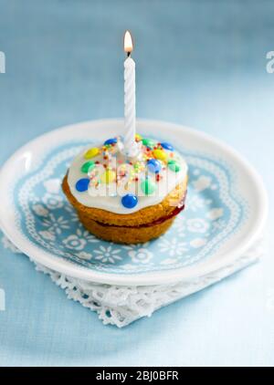 Muffin decorated as a first birthday cake with icin gand single candle burning - Stock Photo