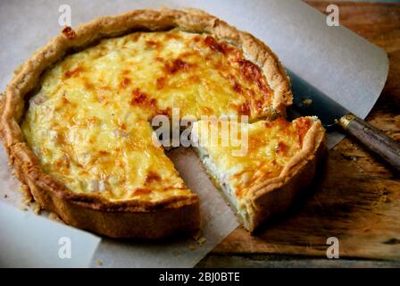 Little Quiche Lorraine on curled greaseproof paper with knife - Stock Photo