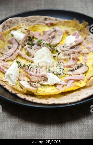 Thin pancake style omelette with mushroom, ham, goat's cheese and parmesan on thin Swedish bread before being rolled up, as a portable breakfast. - Stock Photo