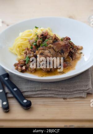 Saddle of rabbit cooked in wine and stock, with shallots, herbs and cherry tomatoes, served with noodles - Stock Photo