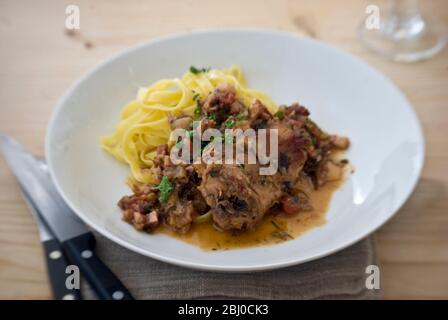 Saddle of rabbit cooked in wine and stock, with shallots, herbs and cherry tomatoes, served with noodles - Stock Photo