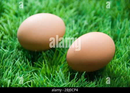 Two brown eggs on fake green plastic grass - Stock Photo