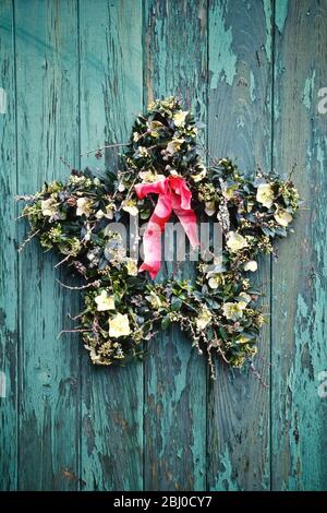 Star shaped wreath made on bent wore coat hangers, hanging on old peeling green door with red ribbon - Stock Photo