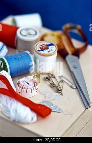 Various bits of sewing kit, including threads, needles and scissors on wooden box. - Stock Photo