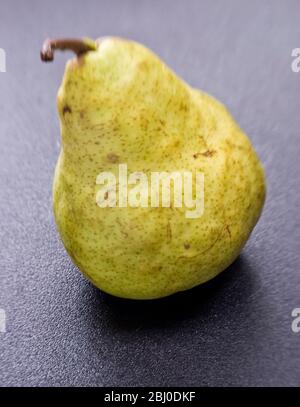 Single yellow green pear on dark surface. - Stock Photo