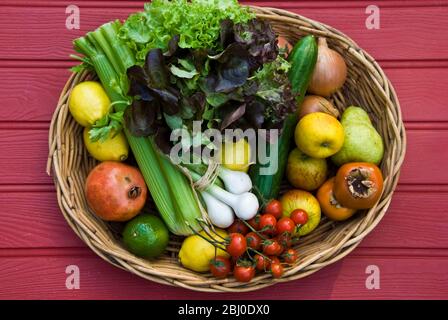 Basket of fresh fruit and vegetables on red surface - Stock Photo