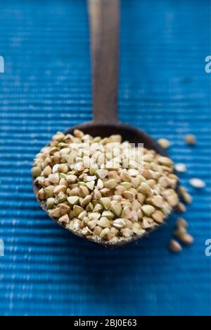 Wooden spoon of whole raw buckwheat grains on blue background - Stock Photo