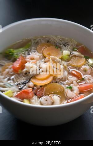 Bowl of asian style soup with rice noodles, prawns, and vegetables - Stock Photo