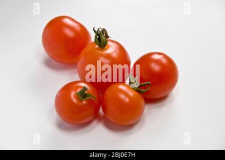 Five red cherry tomatoes on white surface - Stock Photo