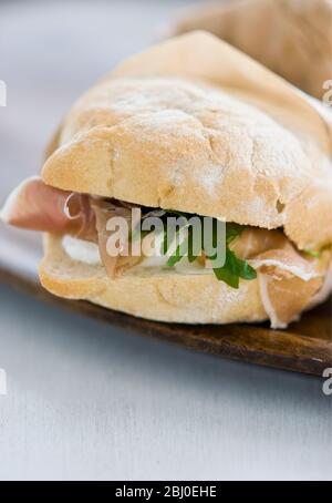 Italian ham sandwich, of parma ham , mozzarella cheese, and frech rocket on light ciabatta type bread, wrapped in greaseproof paper wrapper. - Stock Photo