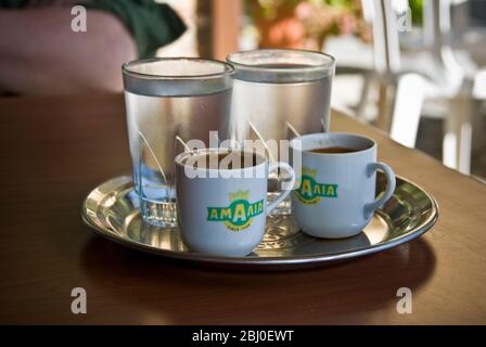 Two little cups of Greek coffee with accompanying glasses of water served in Cypriot cafe in the hills in southern Cyprus - Stock Photo