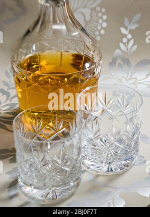 Scotch whisky on ice in cut lead crystal glasses on decorative silver surface, with decanter. - Stock Photo