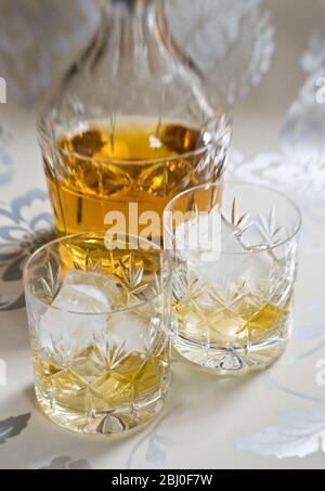 Scotch whisky on ice in cut lead crystal glasses on decorative silver surface, with decanter. - Stock Photo