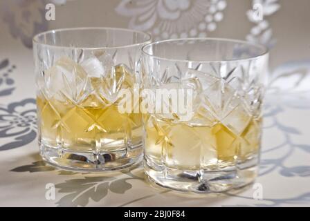 Scotch whisky on ice in cut lead crystal glasses on decorative silver surface - Stock Photo
