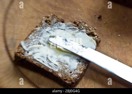 Spreading butter onto slice of Scandinavian style cparse rye bread. - Stock Photo