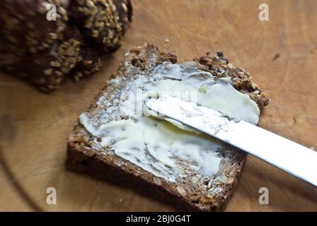 Spreading butter onto slice of Scandinavian style cparse rye bread. - Stock Photo