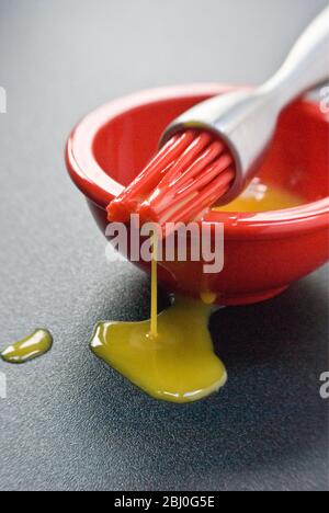 Egg yolk in small red bowl and dripping off red silicone 'bristles' of modern pastry brush. - Stock Photo