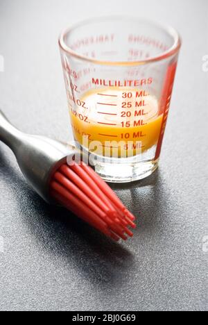 Egg yolk in small glass measuring glass with modern pastry brush with red silicone 'bristles' - Stock Photo