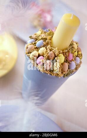 Pastel coloured easter decorations with painted tall pot decorated with sugar coated mini chocolate eggs surrouding candle - Stock Photo