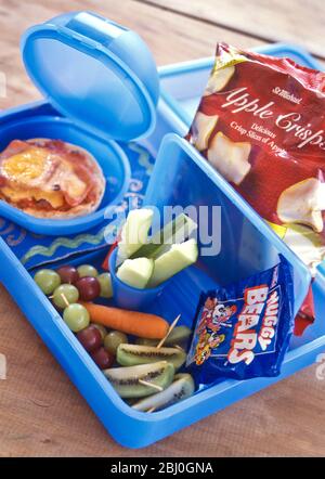 Child's packed lunch of fresh, raw, vegetables, pizza roll and apple crisps, in blue plastic boxes - Stock Photo