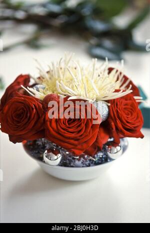 Christmas table decoration of deep red roses and spiky chrysanthemums with silver baubles - Stock Photo