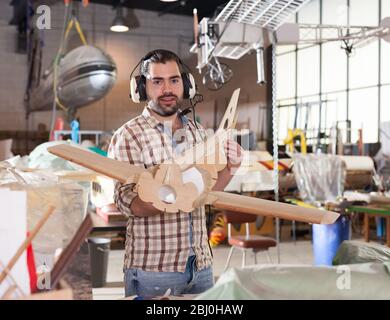 Cheerful male aircraft enthusiast in aviator headphones holding sports airplane models in workshop Stock Photo