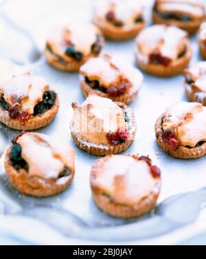Little mince pies decorated with pastry holly leaves and cranberries dusted with icing sugar, on metal tray - Stock Photo