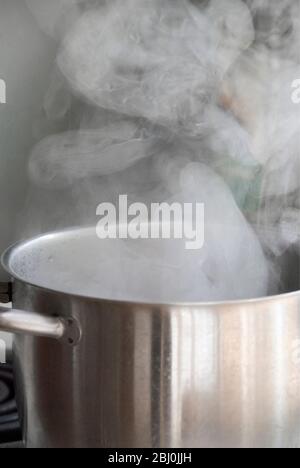 Steam from water boiling in stainless steel saucepan on hob - Stock Photo